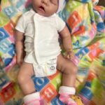 Realistic full body silicone baby girl doll Ellie posed sleeping on a pink cushion.