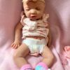 Realistic full body silicone baby girl doll Ellie posed sleeping on a pink cushion.