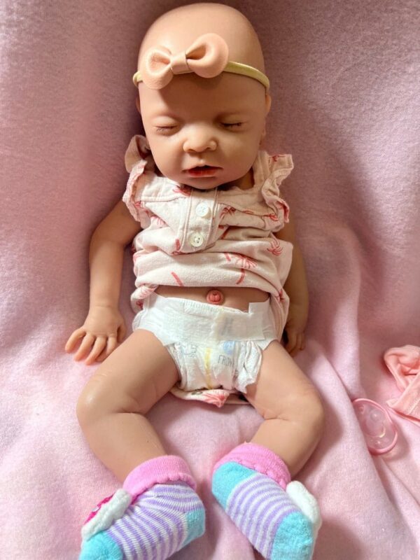 Realistic full body silicone baby girl doll Ellie posed sleeping on a pink cushion.