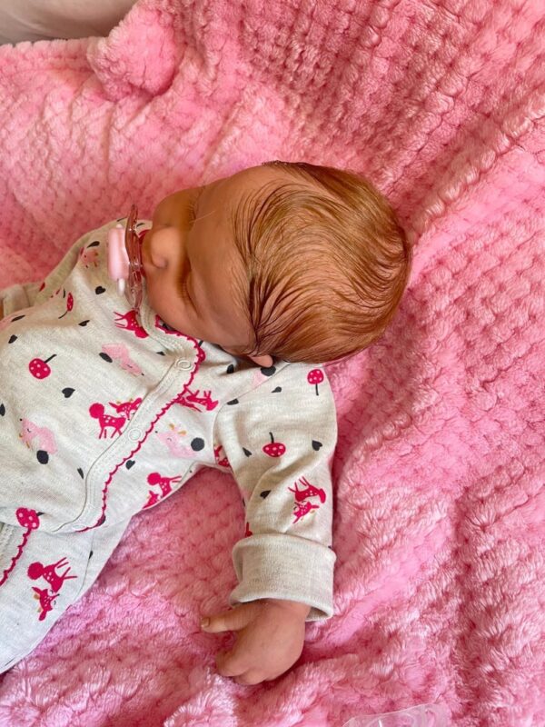 Full silicone reborn baby doll Lucy sleeping soundly in a striped knit outfit.