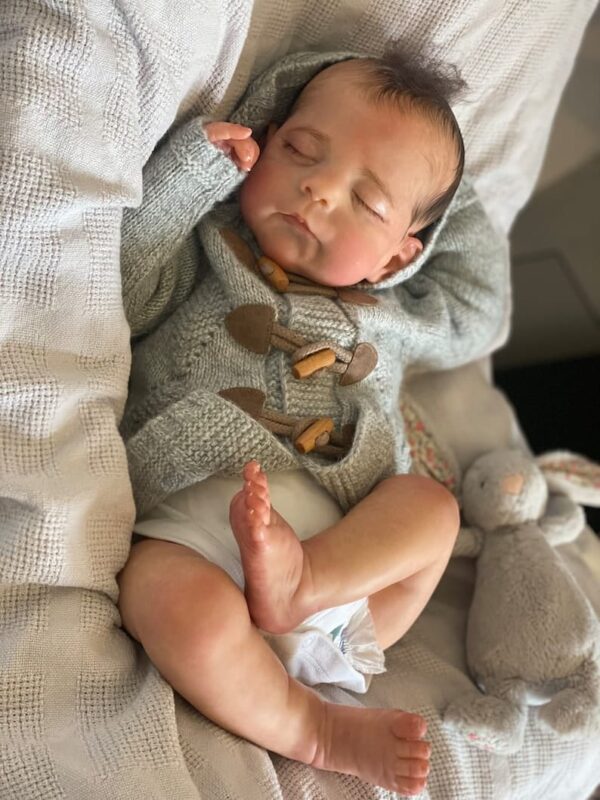 Lifelike reborn baby boy doll Eric with hand-rooted brown hair, dressed in a blue button-up outfit.