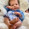 Realistic reborn baby girl doll Evelyn with brown hair and a gentle expression, wearing a ruffled white dress.