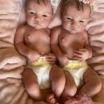 Ultra-realistic full body silicone twin baby dolls, Daisy and Riley, awake and smiling.