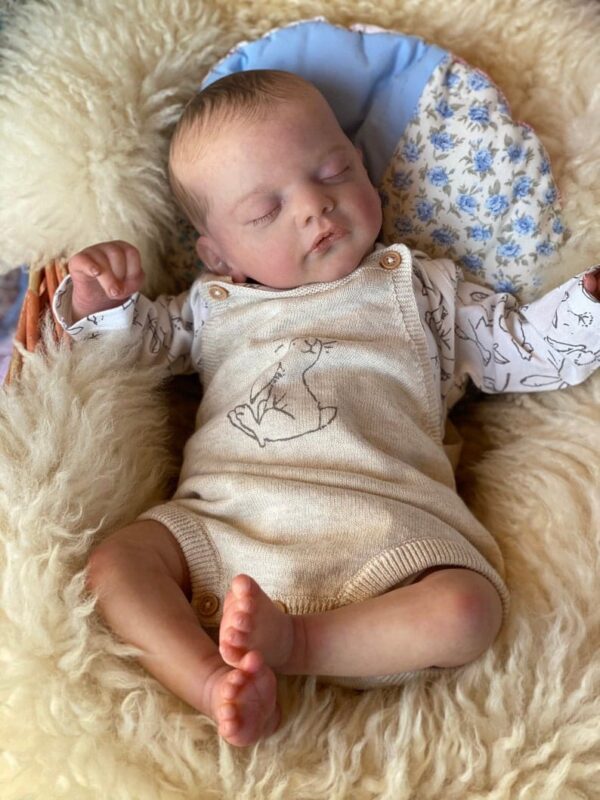 Lifelike vinyl reborn baby boy doll Aiden, dressed in a blue sleeper and sleeping peacefully.