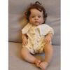 Realistic vinyl reborn baby doll Hazel with bright eyes and hand-rooted hair, sitting in a floral dress.