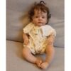 Realistic vinyl reborn baby doll Hazel with bright eyes and hand-rooted hair, sitting in a floral dress.